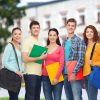 friendship, school, education and people concept - group of smiling teenagers with folders and school bags over campus background